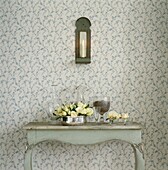 Yellow roses on painted side table with wall-mounted candle holder on floral wallpaper