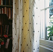 Cream patterned silk curtains at window with bookcase