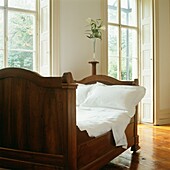 Wooden bed in living room with polished wooden floors and shutters at French windows