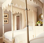 Cream four poster bed in neutral bedroom with convex mirror