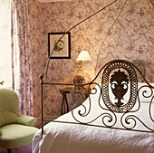 Ornate metalworked footboard in bedroom with co-ordinated wallpaper and curtains