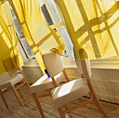 Drei cremefarbene Esszimmerstühle am Fenster mit gelben Vorhängen