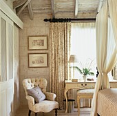 Cream coloured bedroom with armchair and table at window and fabric on four poster bed