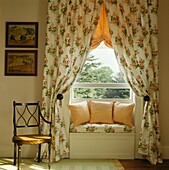 Floral patterned curtains co-ordinating with window seat in room with chair and artwork
