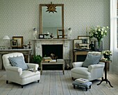 Matching armchairs with co-ordinated checked fabric in living room with patterned wallpaper and painted floorboards