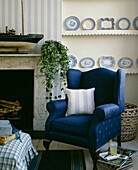 Striped cushion on blue upholstered armchair at fireplace with model boat and ivy
