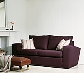 Deep purple sofa with cushions and leather footstool in white panelled room