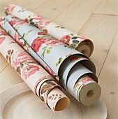 Three rolls of floral patterned wallpaper on exposed wooden floorboards