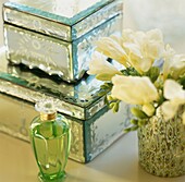 Perfume bottle and cut flowers with jewellery boxes on dressing table