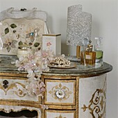 Artificial flowers and scent bottles with silver lampshade on ornate hand-painted dressing table