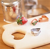 Pastry cutters and strawberry on chopping board with metal storage jars