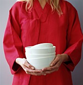 Mid section woman in pink holding stack of white china bowls