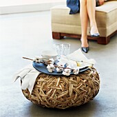 Tray with crockery on woven footstool ladies legs in background