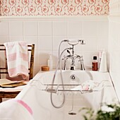 Shower fitting on bath below floral patterned wallpaper