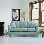 Pale blue sofa in living room with white painted floorboards and stripped wood window