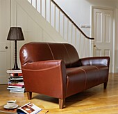 Brown leather sofa and pile of books with lamp in sparsely furnished open plan reception room