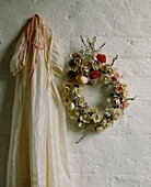Christening gown hanging with wreath on whitewashed wall