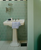 Keramisches Waschbecken in einem grün gefliesten Badezimmer mit Klappspiegel