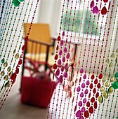 Multi color beaded curtain with chair and basket behind