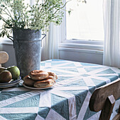 Bagels and apples and wild flowers on patchwork tablecloth beside a window in kitchen