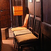 Clutter of wooden chairs with silk cushion covers in panelled hallway 