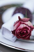 Place setting with a deep pink rose placed next to a white napkin