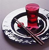 Karminrosa Glasbecher und Essstäbchen auf glänzender versilberter Platte