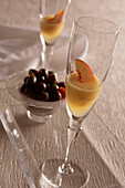 Zwei Gläser Bellini, Champagner mit pürierten Pfirsichen und Pfirsichlikör auf einem Glastablett mit einem Teller mit Oliven