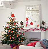 White living room with a colourful christmas tree decorated in an oriental theme tied with gift bags and lanterns in orange and pink 