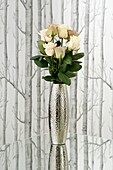 metal vase on reflective mirrored table top with fresh roses against Tree Silhouette wallpaper