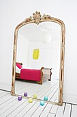 Oversized ornate vintage mirror in all white bedroom with sleigh bed and wardrobes reflected in the mirror and colourful accessories