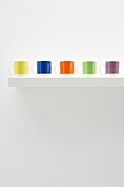 Five brightly coloured cups on a white shelf