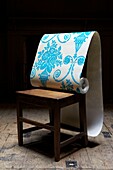 Dramatic shot of a roll of blue and white flock wallpaper on a wooden chair