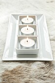 White ceramic tray with 3 lit tealights on a fur throw