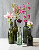 Rosa, einstielige Blumen in alten Glasflaschen