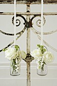 Vintage-Geländer aus Eisen mit weißem Blumenschmuck in einem Glasgefäß, das an weißen Bändern hängt