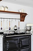 Black range oven with utensils hanging under wooden shelf