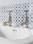 Old fashioned metal taps on washbasin with tiled splashback