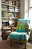 Checked blanket on armchair beside bookshelf with sewing machine
