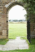 View through paved stone archway with gate to grass field