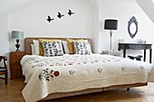 Flying ducks over bed with quilted cover and butterfly motif cushions in London home   UK