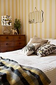 Vintage mirror hangs on striped wallpaper in bedroom with assorted grey and yellow patterns   London home   UK