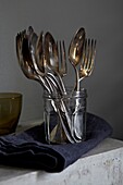 Vintage silver spoons and forks in a jamjar with denim napkin