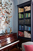 Piano and bookcase with wall poster of birds in Tiverton country home,  Devon,  England,  UK