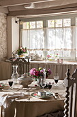 Dining table with net curtains at window in stone farmhouse,  Dordogne,  France