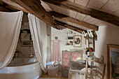 Cream curtains around corner bath in beamed attic bathroom of Dordogne farmhouse,  France