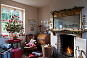 Geschnitzter Holzspiegel über beleuchtetem Feuer im Wohnzimmer eines Bauernhauses in Tiverton mit Weihnachtsbaum Devon UK