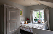 Kinderzimmer in Grau mit Kuscheltieren auf dem Bett und grauem Kleiderschrank