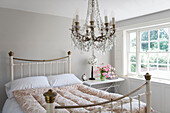 Glass chandelier above metal bed with quilted duvet  at window in Kent home  England  UK