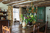 Cut flowers and chandelier with dining table and low beamed ceiling in Ashford farmhouse  Kent  UK